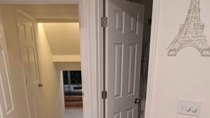 Un pasillo con piso de baldosas, puertas blancas y un interruptor de luz en la pared.