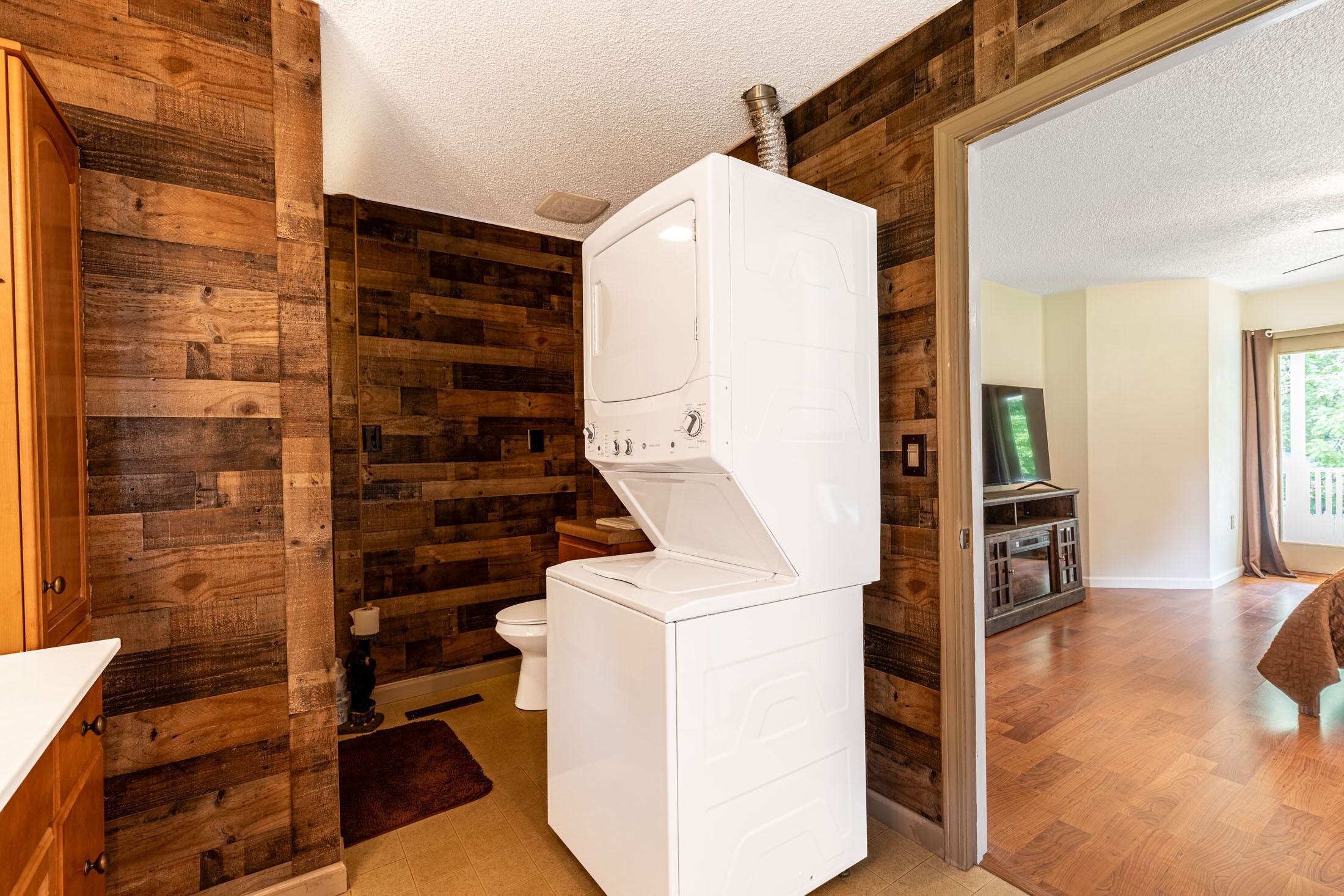 A compact laundry room with a built-in washer and dryer, wooden wall paneling, a toilet, and a small rug.