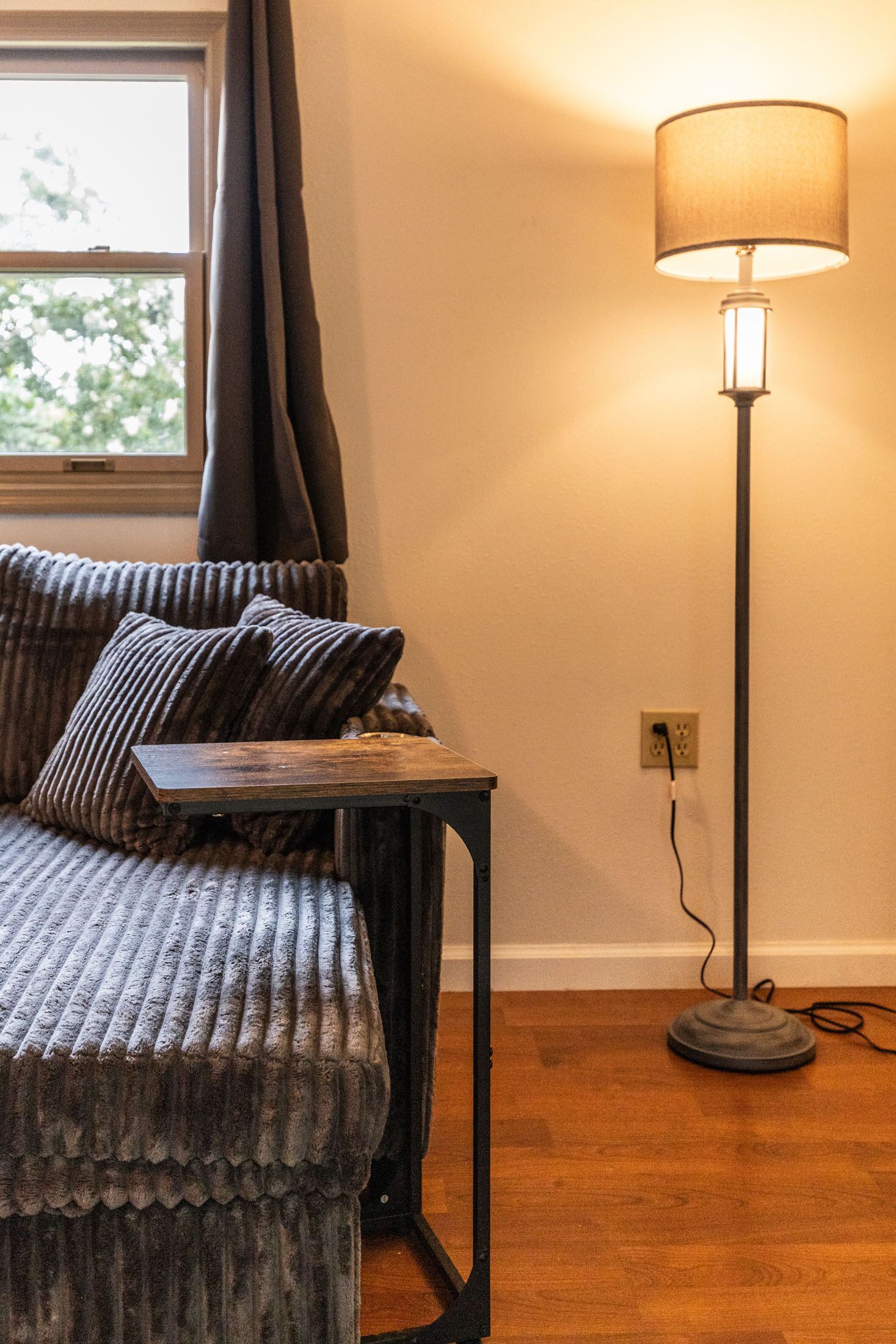 Ett rum med en soffa, ett bord, en lampa och ett fönster.