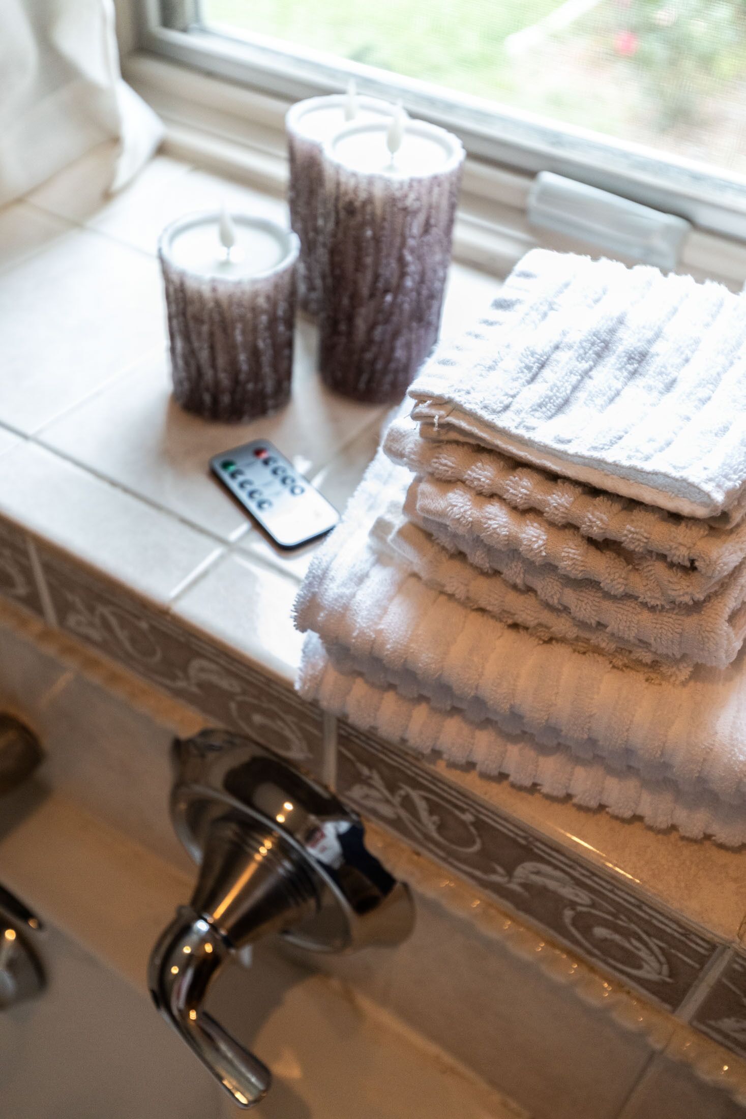 A bathroom with a window, a remote control, and a stack of towels.