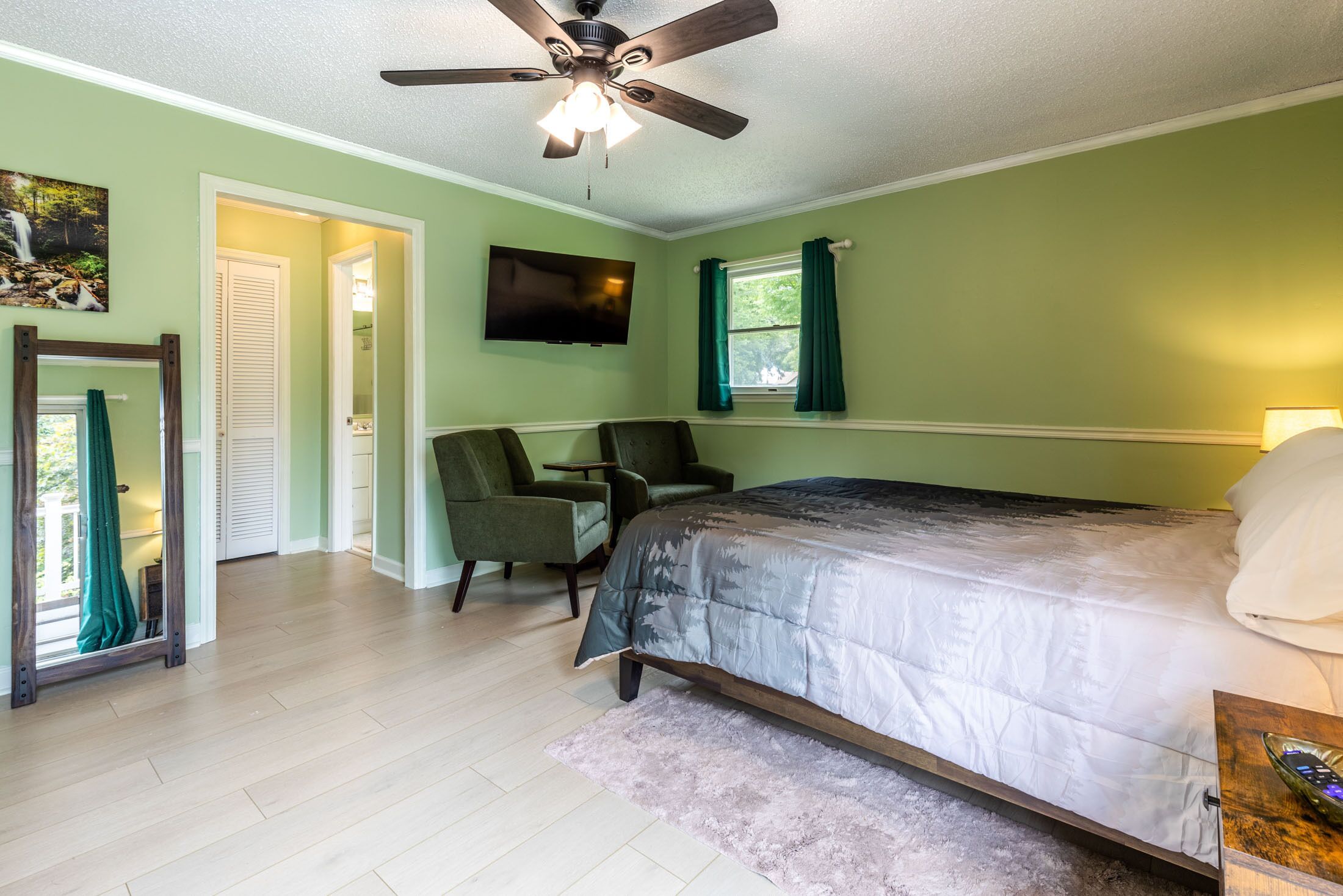 A bedroom with a bed, a desk, a chair, a television, and a ceiling fan.