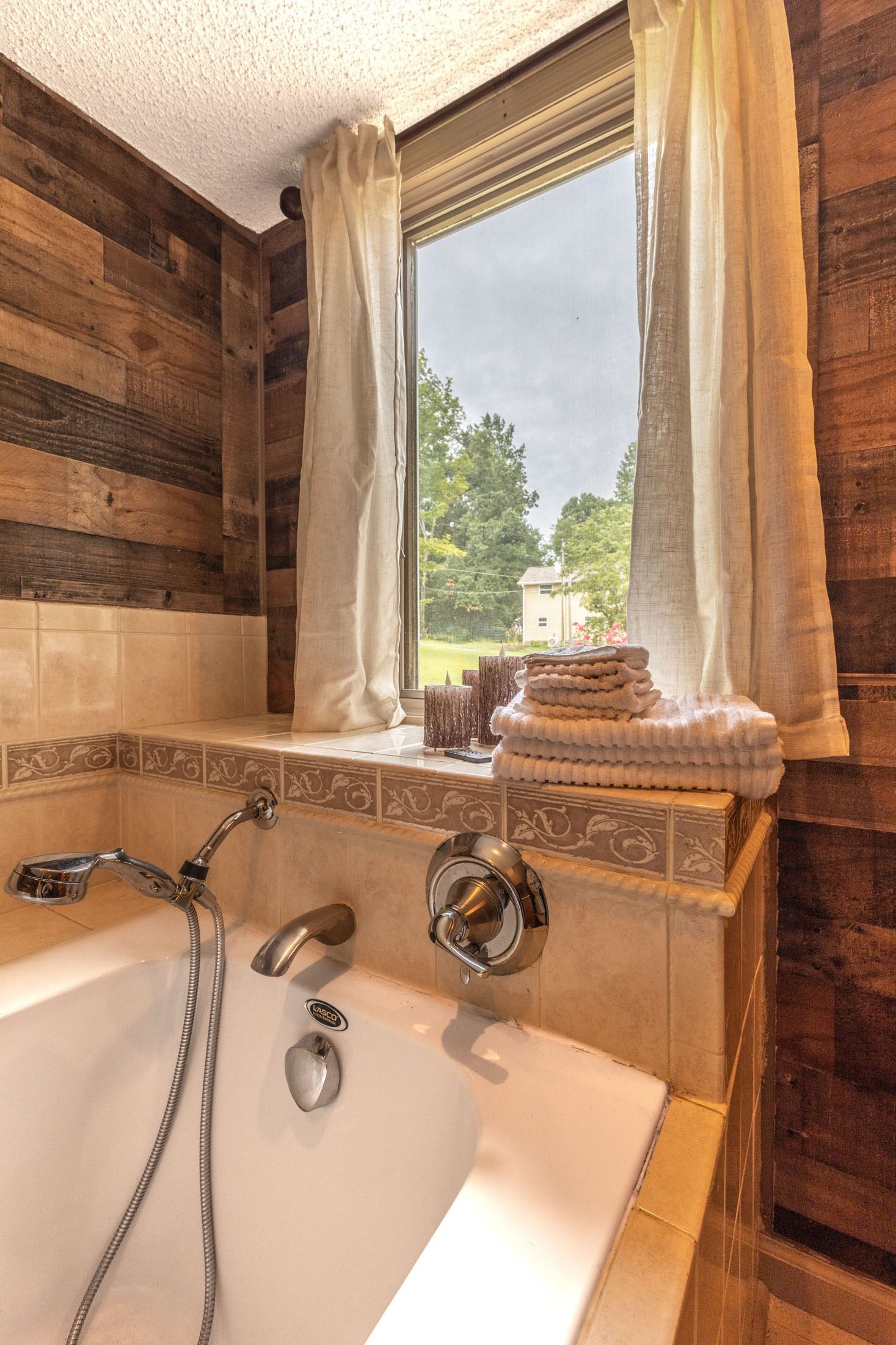 A bathroom with a bathtub, two showerheads, and a window with curtains.