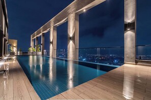 A rooftop infinity pool with a city view at night, supported by concrete columns, and wooden flooring. -  SKHomes, modern apartment with city views (Nairobi)