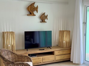 Una sala de estar con televisor de pantalla plana, mueble de entretenimiento de madera, una silla de mimbre y dos adornos de madera colgados en la pared.