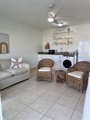 Una cocina moderna con armarios blancos, microondas y cafetera. Hay sillas de mimbre y un sofá con almohadones en forma de estrella.
