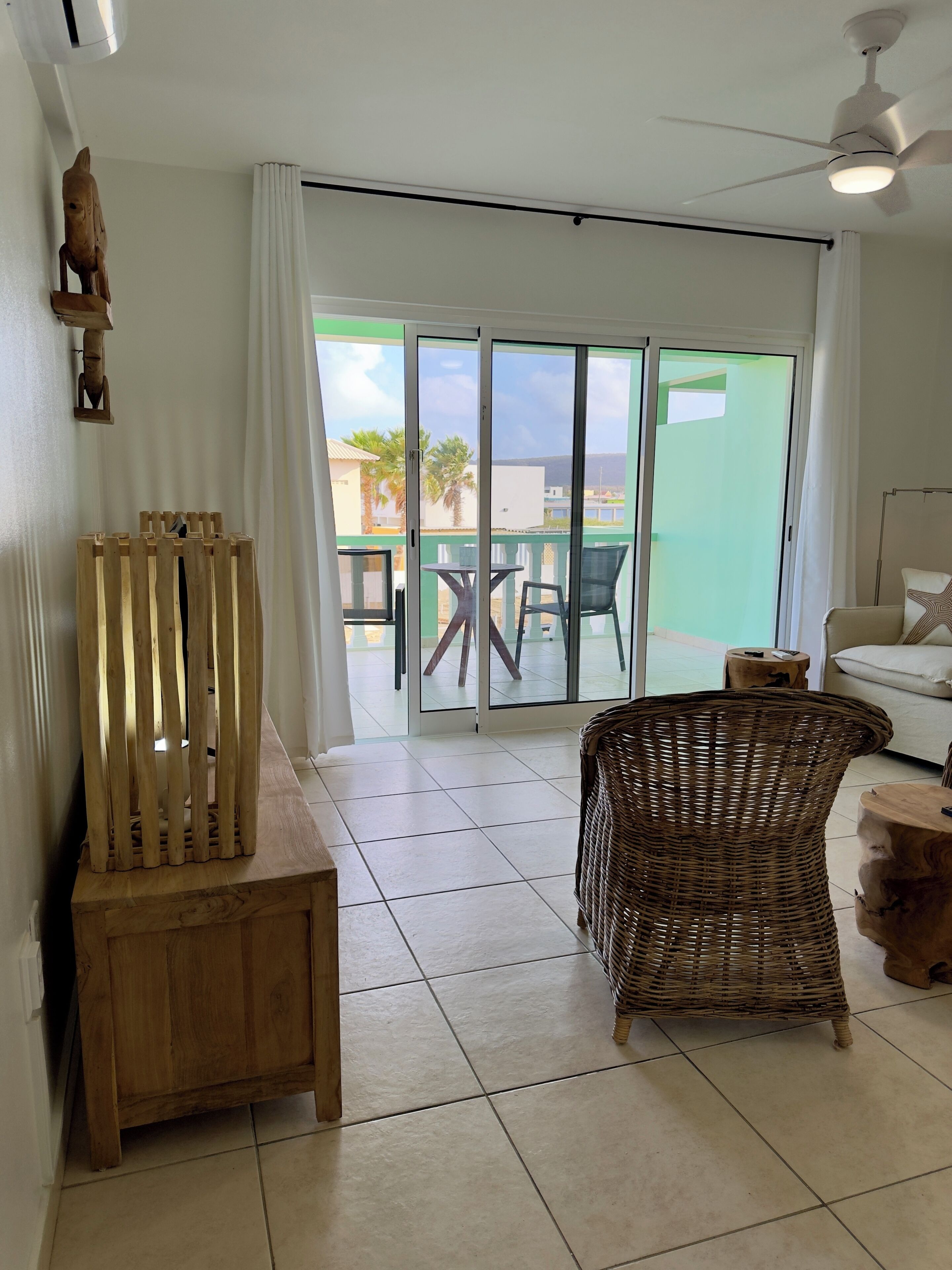 A room with a wooden chair, a wicker chair, a sofa, a small table, and a ceiling fan.