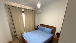 A bedroom with a wooden bed, a nightstand, a lamp, and an air conditioning unit. - Nour 5 Modern Apartment with Pool & Parking Near Train Station Central Marrakech (Marrakesh)