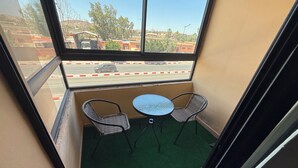 A small balcony with two wicker chairs and a round table, overlooking a street with buildings and trees. - Nour 5 Modern Apartment with Pool & Parking Near Train Station Central Marrakech (Marrakesh)