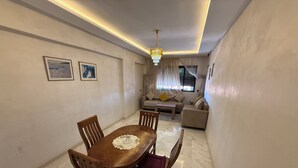 A dining area with a wooden table and chairs, a chandelier, and a sofa in the background. - Nour 5 Modern Apartment with Pool & Parking Near Train Station Central Marrakech (Marrakesh)