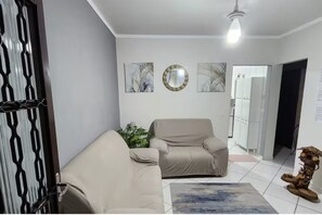 Una sala de estar con un sofá color beige, una butaca, una mesita y una planta decorativa.