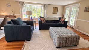 Ein Wohnzimmer mit einer Couch, einem Hocker und einer Lampe auf einem Tisch.