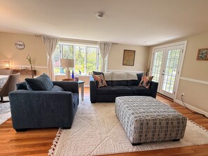 Ein Wohnzimmer mit einer Couch, einem Hocker und einer Lampe auf einem Tisch.