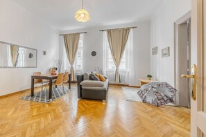 Ein Zimmer mit Holzboden im Fischgrätmuster, einer Couch, einem Esstisch mit Stühlen, einer Hängeleuchte und einer Tür mit goldener Griff.