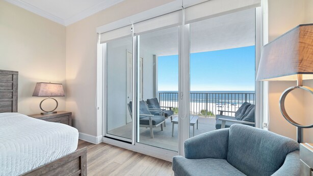 Een slaapkamer met een bed, een stoel, een lamp en een glazen schuifdeur naar een balkon met stoelen en een tafel.