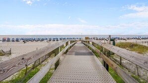Une promenade en bois menant à une plage où se trouvent des parasols bleus et des chaises de plage.