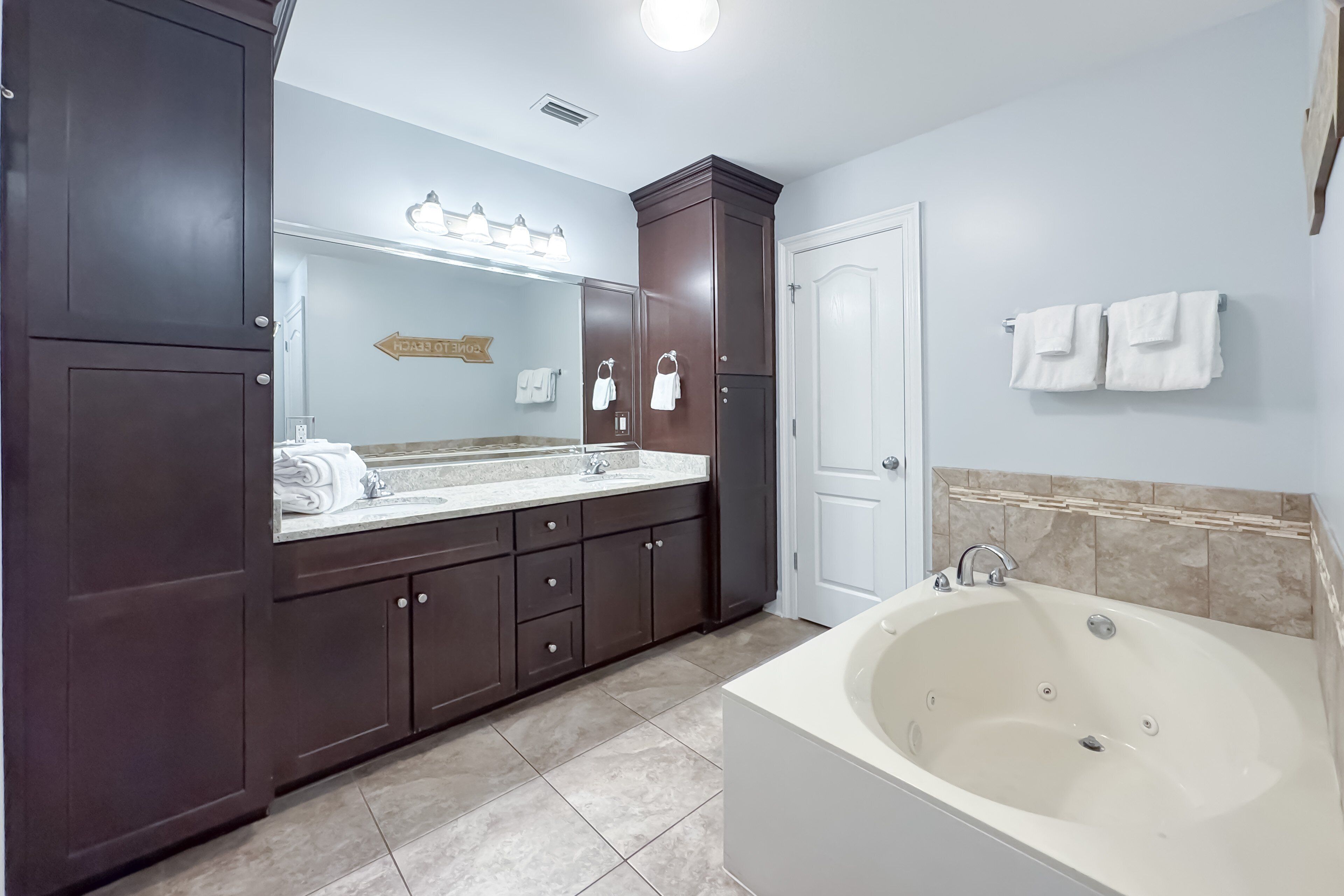 Une salle de bain avec une baignoire, un lavabo et un miroir. Des serviettes sont accrochées au mur et il y a un meuble avec des tiroirs.