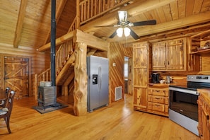 A log cabin interior with a wooden staircase, a refrigerator, a stove, and a kitchen area.