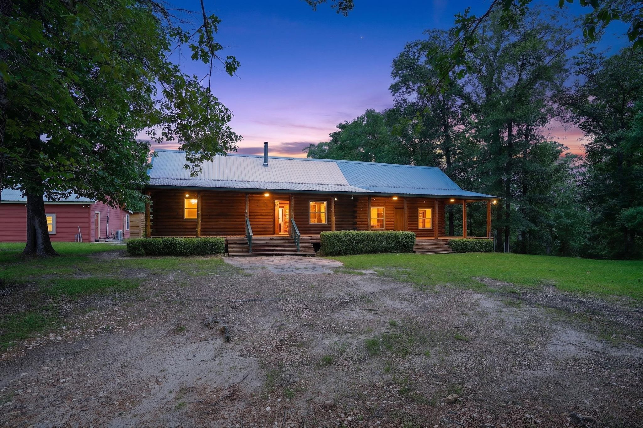 A wooden cabin with a metal roof, surrounded by trees and a gravel driveway.