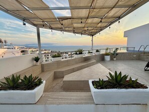 Eine Dachterrasse mit Topfpflanzen, einem Pool und Blick aufs Meer.