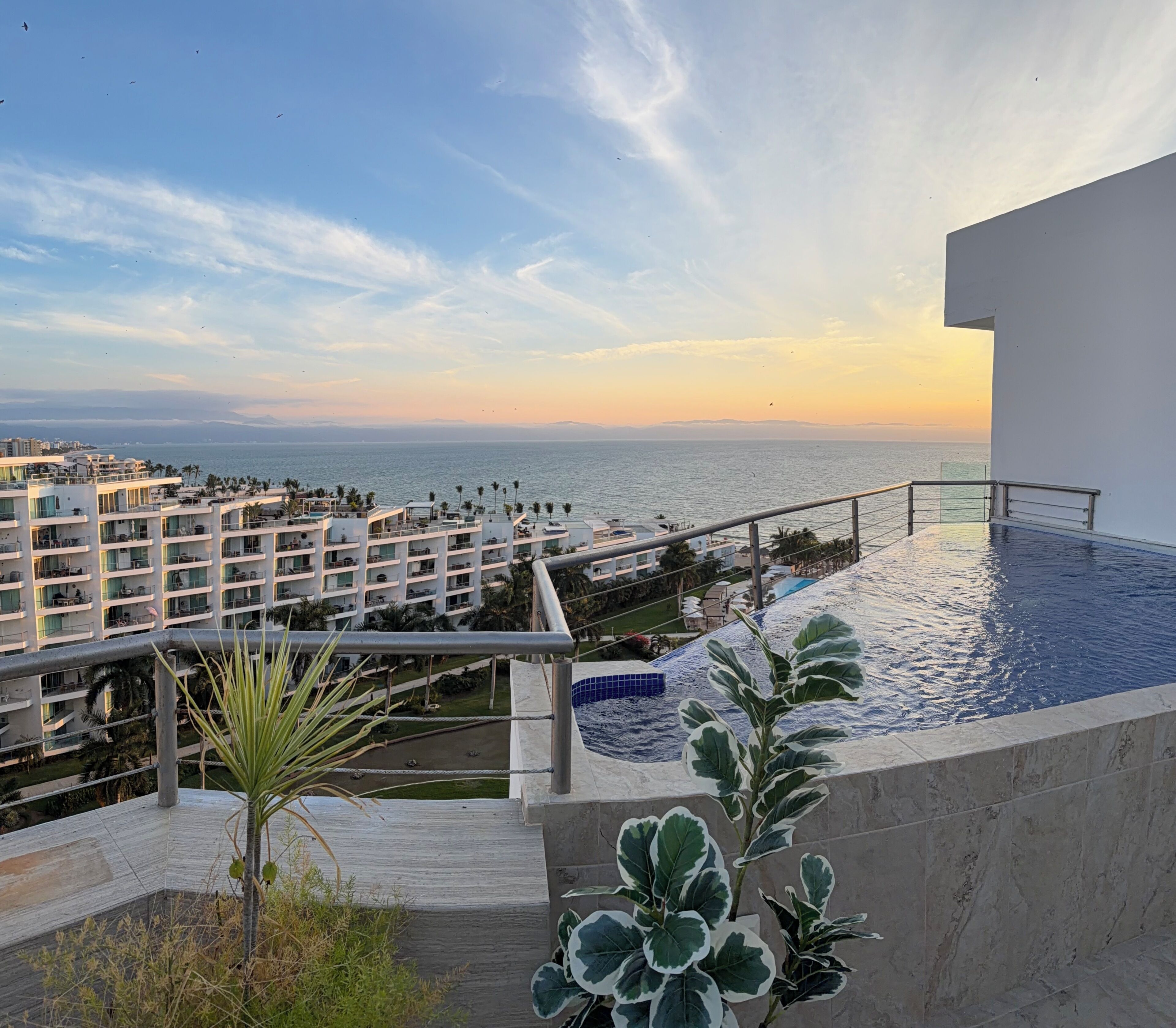 A hotel with a pool, a view of the sea, and a balcony with plants.