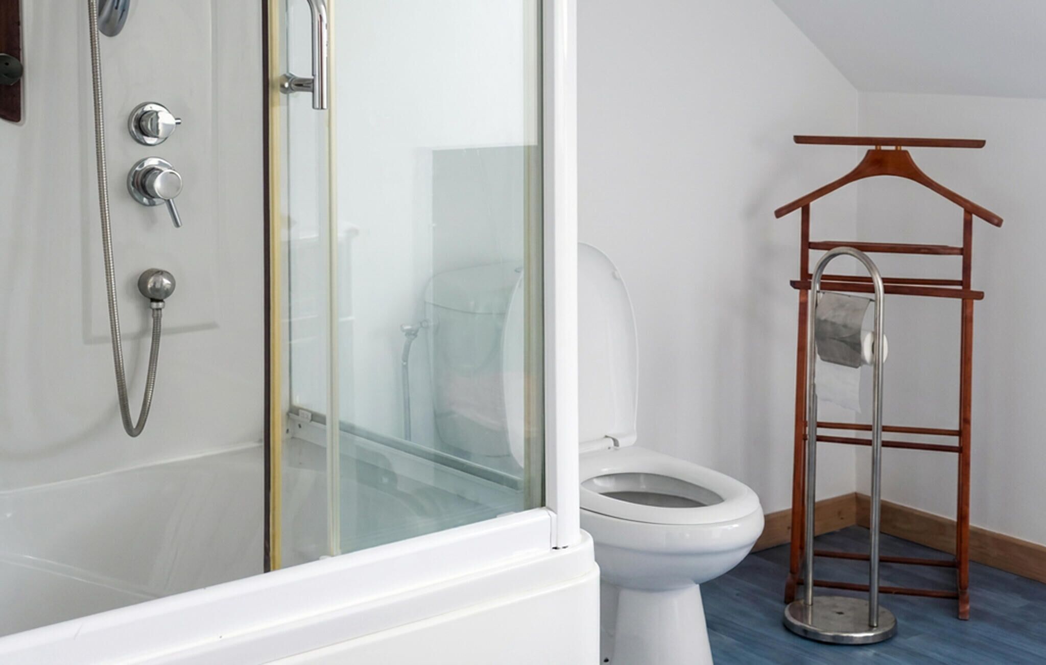 Et badeværelse med bruser, toilet og et træstativ til tøj.