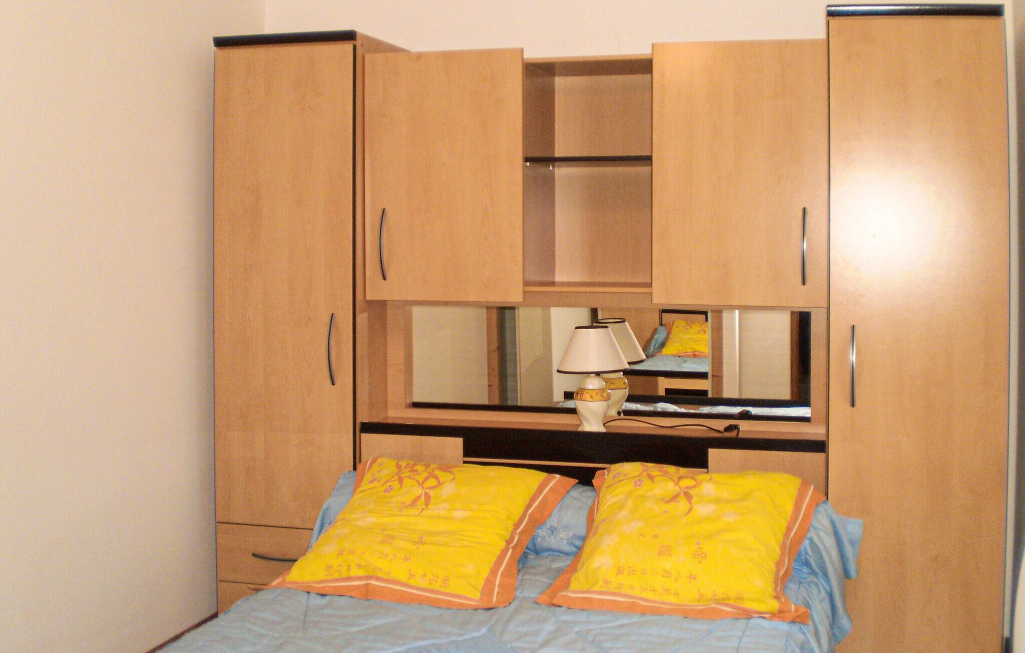 Ein Schlafzimmer mit einem Bett, zwei Kissen, einem Nachttisch mit Lampe und einem Holzschrank mit mehreren Fächern.