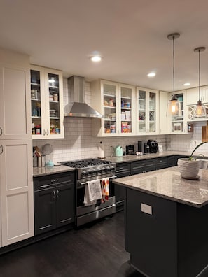 A modern kitchen with white cabinets, a stainless steel stove, and a granite countertop. - World Cup Rental Near Mercedes-Benz Stadium Renovated 3BR Atlanta Home (Atlanta)