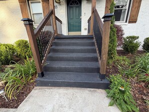 A set of black stairs with wooden railings leading to a green door, surrounded by greenery and a white brick wall. - World Cup Rental Near Mercedes-Benz Stadium Renovated 3BR Atlanta Home (Atlanta)