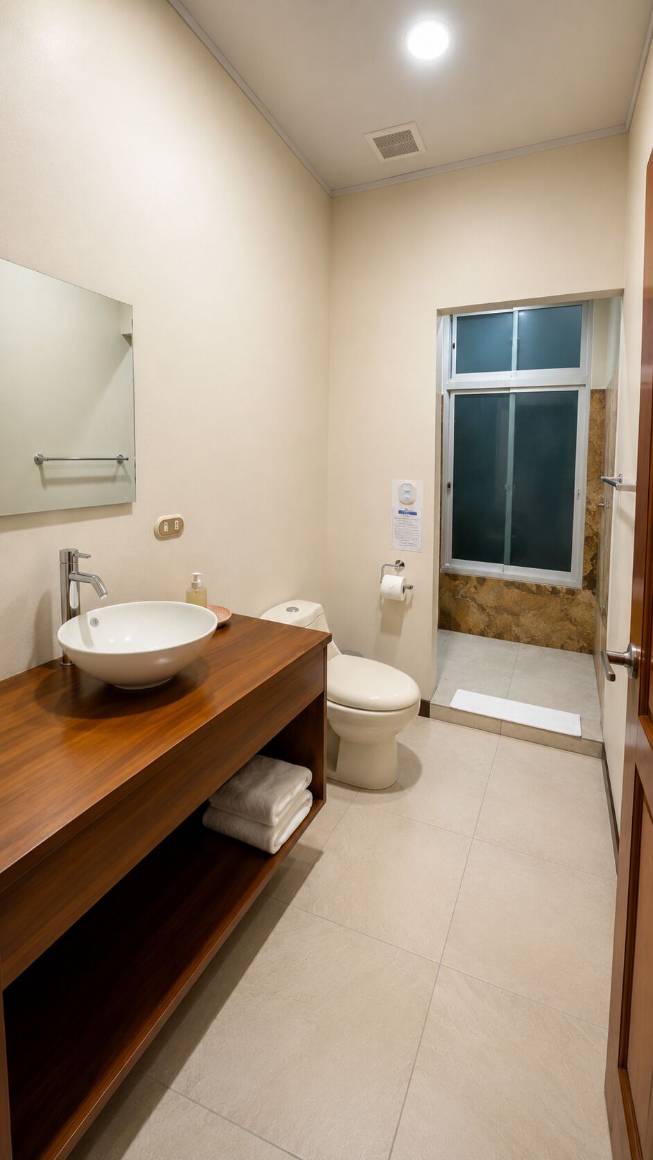 A modern bathroom with a wooden vanity, a white sink, a toilet, and a shower area with a glass door.