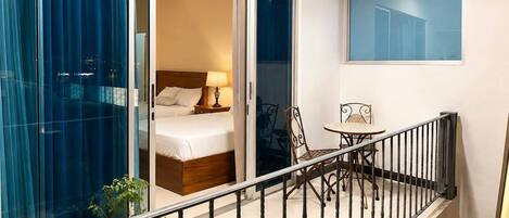 A balcony with a bed, a table, chairs, and a potted plant.