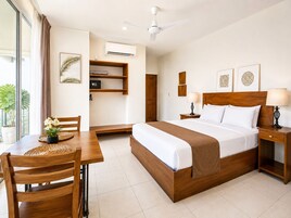 Habitación de hotel con cama, mesitas de noche, un escritorio con silla, ventilador de techo y ventana con cortinas.