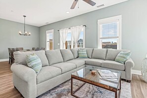 Un salon avec un canapé d’angle, une table basse en verre et un ventilateur de plafond.