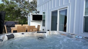 Un jacuzzi en el exterior de una casa con una terraza de madera y sillas.