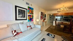 A living room with a sofa, a coffee table, and a dining area with a table and chairs. - Urban One Retreat (Miami)
