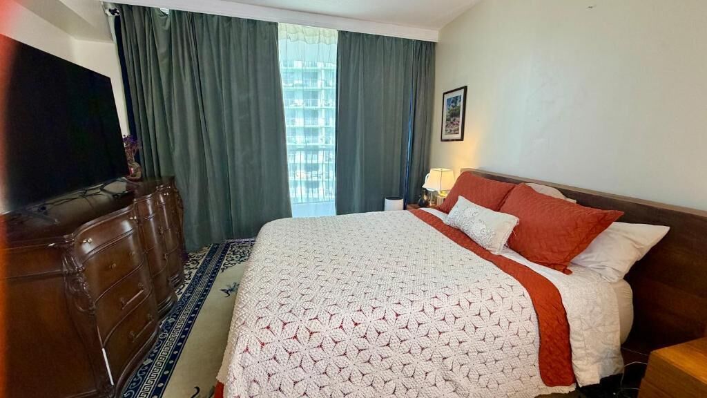 A hotel room with a large bed, a dresser, a television, and a window with curtains.
