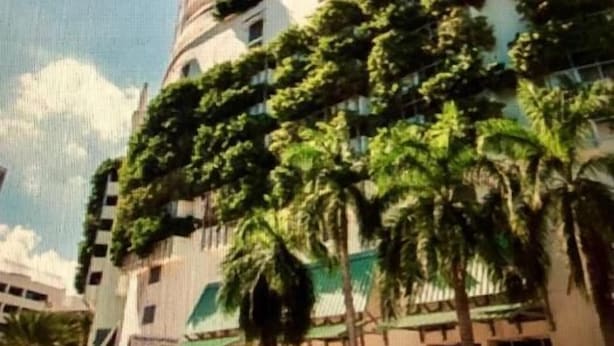 A tall, cylindrical building with a modern design, surrounded by lush greenery and palm trees. - Urban One Retreat (Miami)