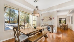Ein Essbereich mit Holztisch, Bänken und Stühlen, einer Chandelierleuchtre und Blick ins Freie.