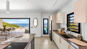 Una cocina moderna con vista al mar, un comedor con mesa para dos, y una pequeña isla con estufa integrada.
