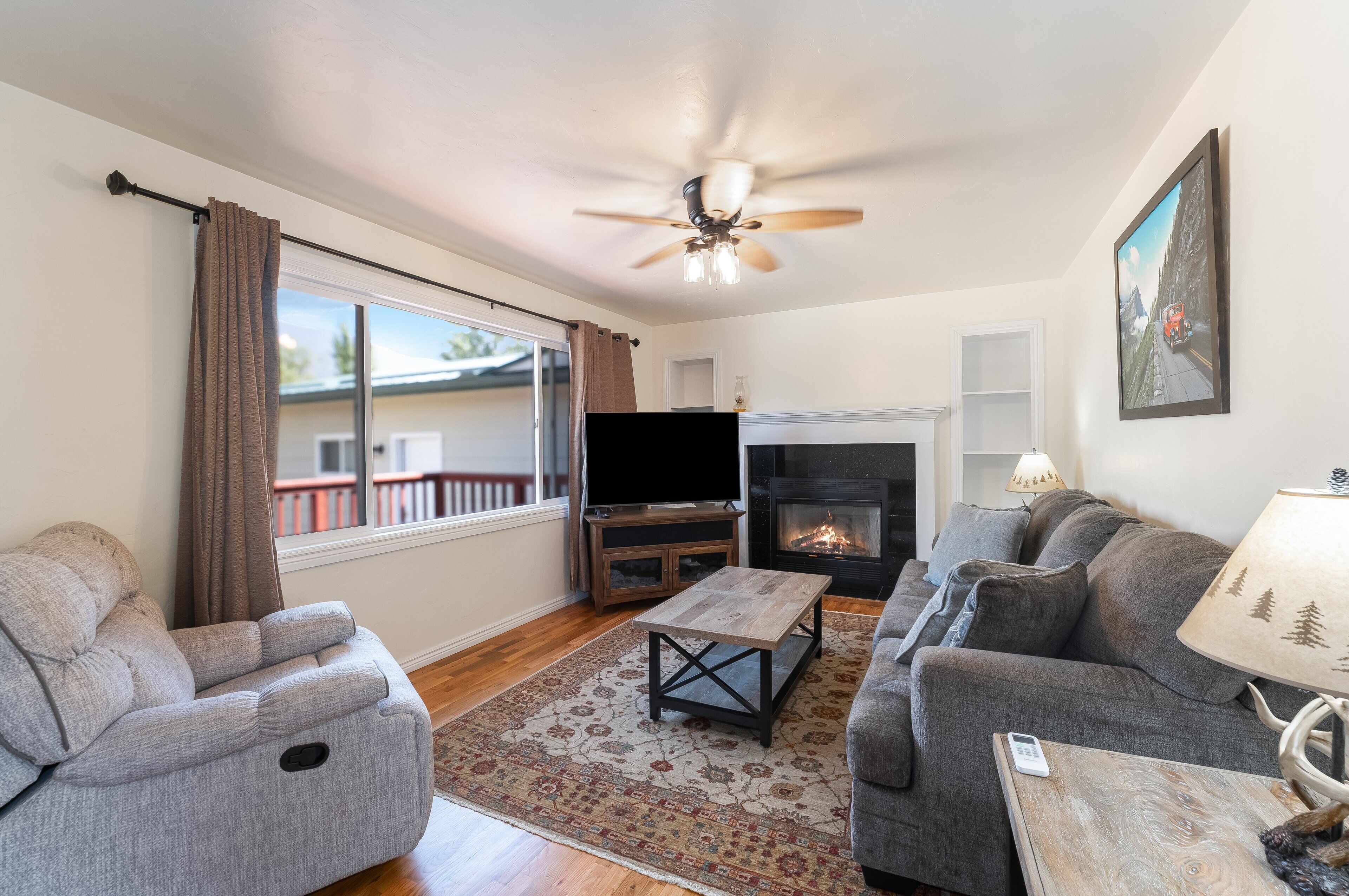 A living room with a fireplace, a television, and a ceiling fan.