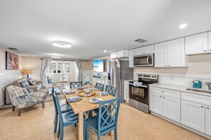 Una cocina moderna con armarios blancos, electrodomésticos de acero inoxidable y un comedor con sillas azules y una mesa de madera.