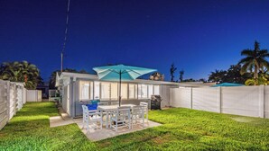 Un jardin avec une table et des chaises de patio, un barbecue et un parasol bleu.