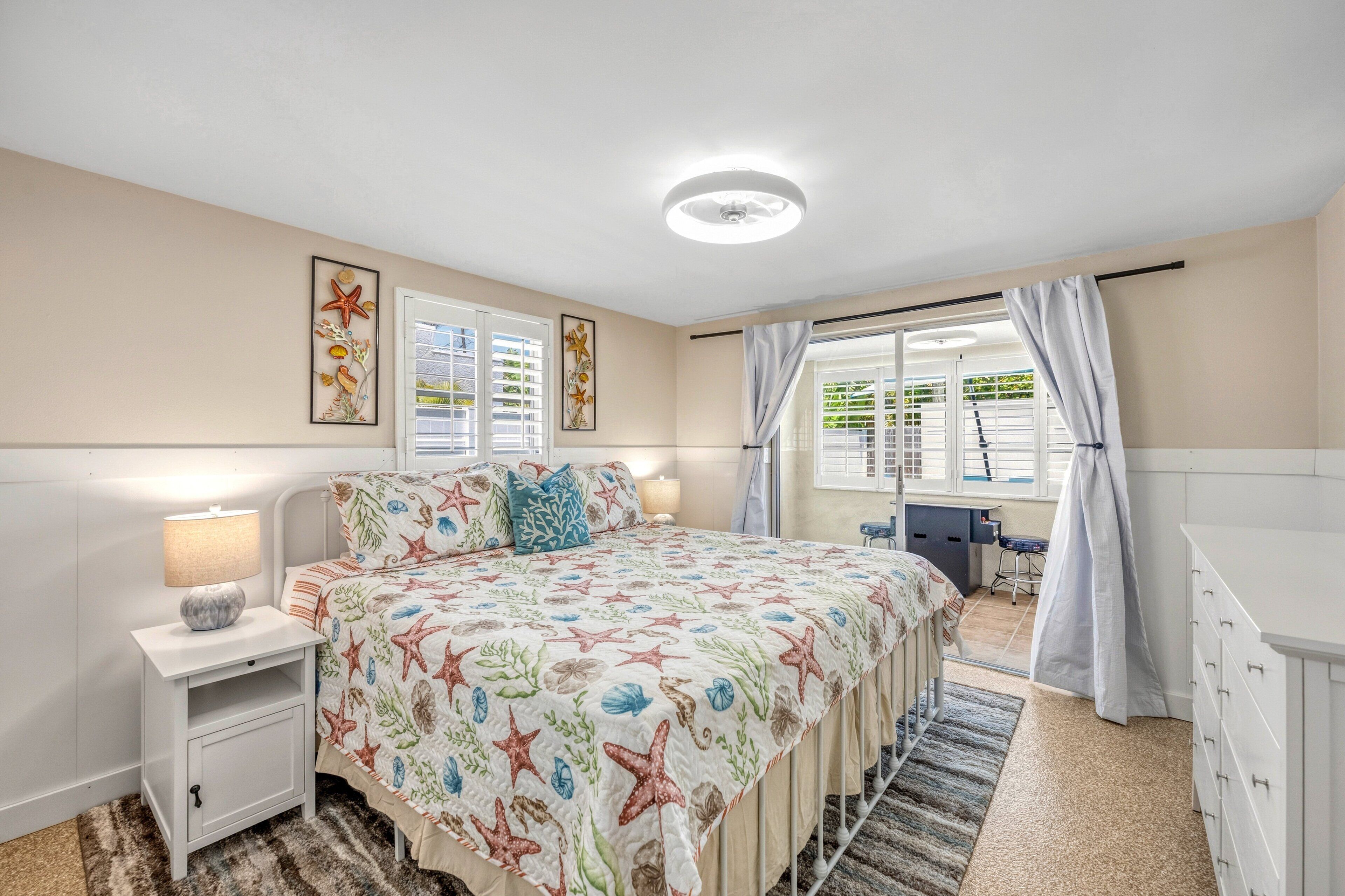 A bedroom with a bed, nightstand, lamp, and a view of the outside.