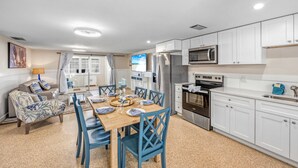 Une cuisine moderne avec des meubles blancs, des appareils en acier inoxydable et un coin repas avec des chaises bleues et une table en bois.