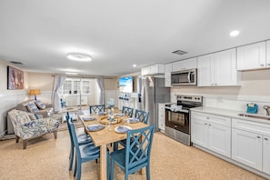 A modern kitchen with white cabinets, stainless steel appliances, and a dining area with blue chairs and a wooden table. - Key Life Sands | Duplex Unit Near Crescent Beach with Private Outdoor Living (Sarasota)