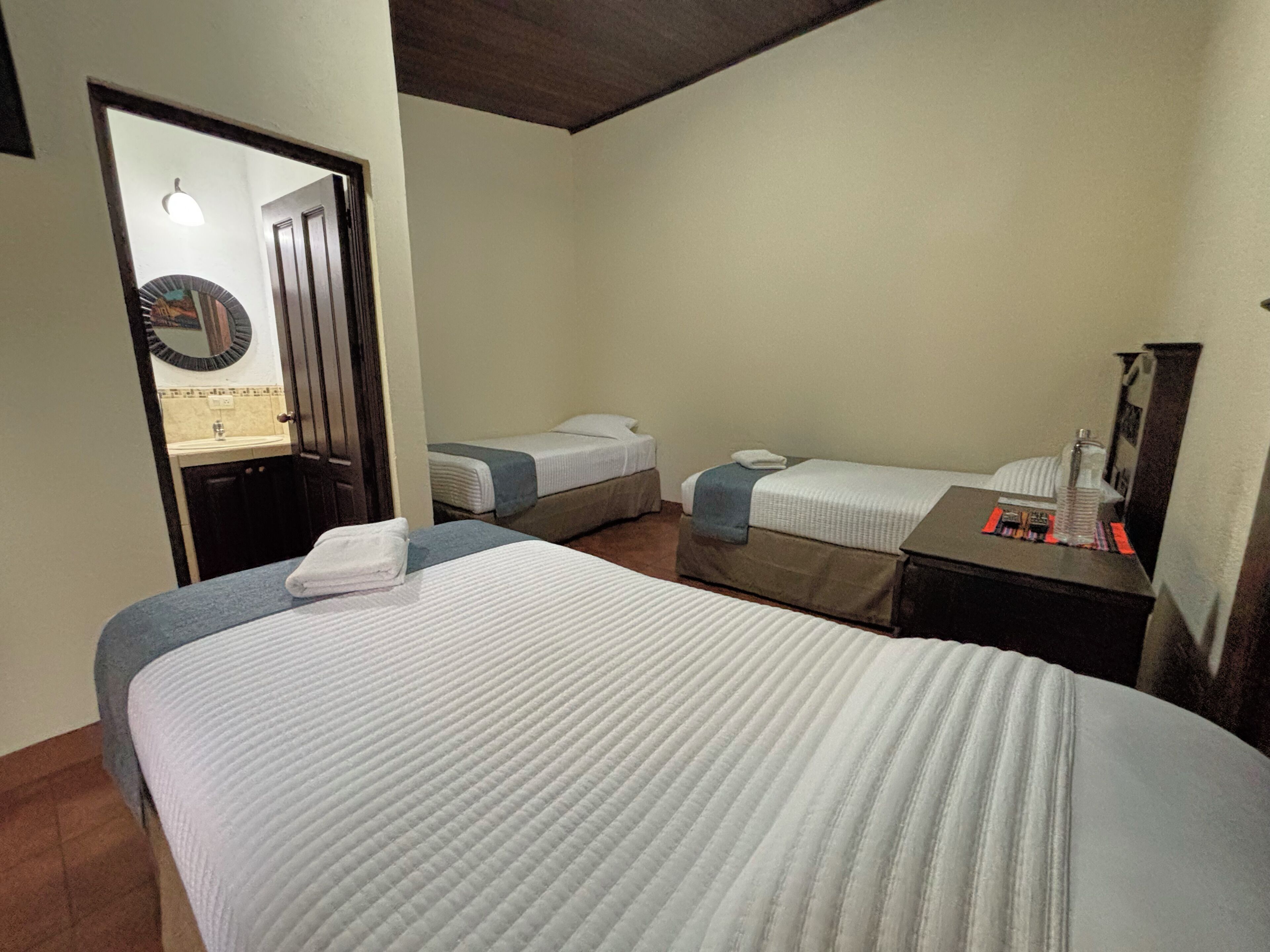 A hotel room with two beds, a small table with toiletries, a mirror, and a door leading to a bathroom.
