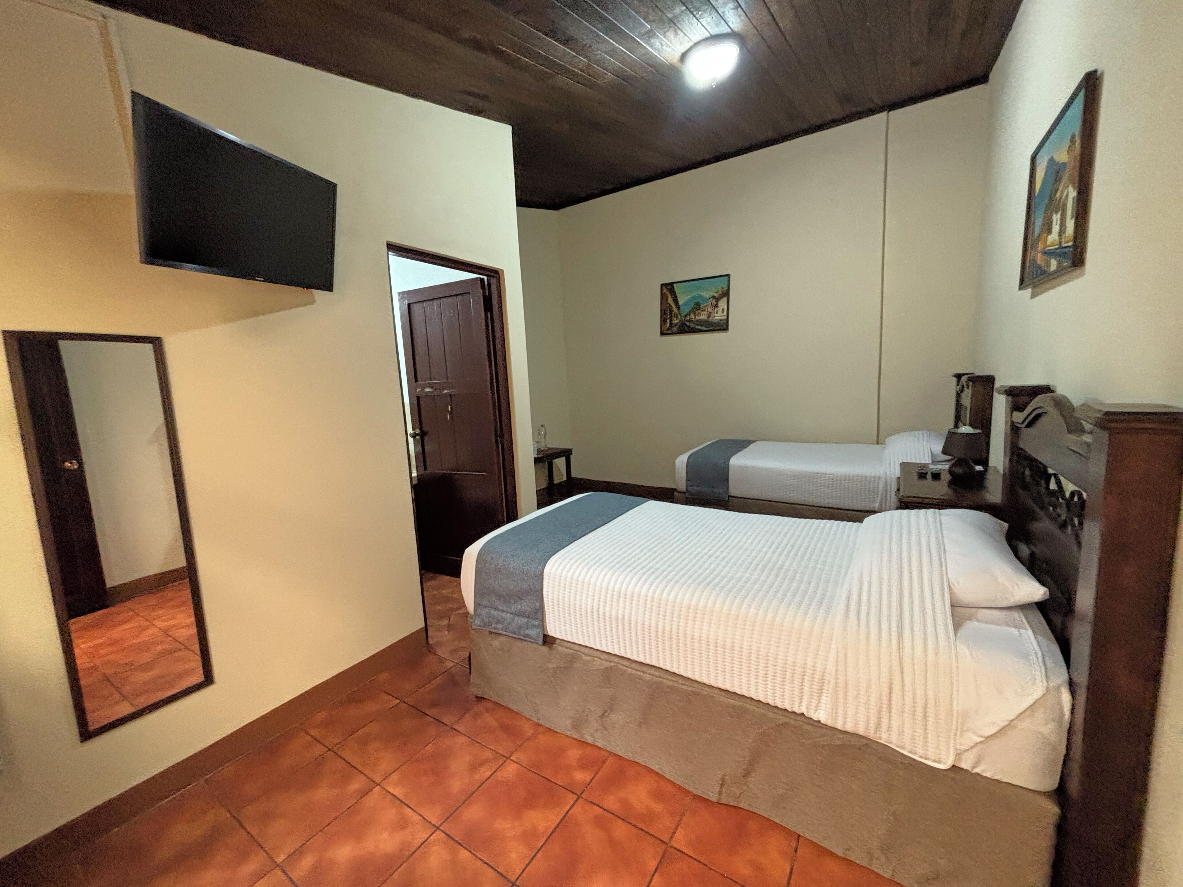 Un dormitorio con dos camas, techo de madera, un cuadro en la pared y una puerta que da a otra habitación.