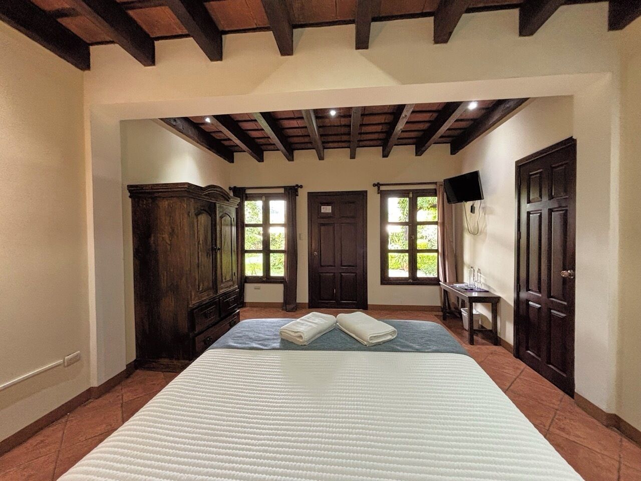 Une chambre d’hôtel avec un grand lit, une armoire en bois, un bureau avec une chaise et un téléviseur.