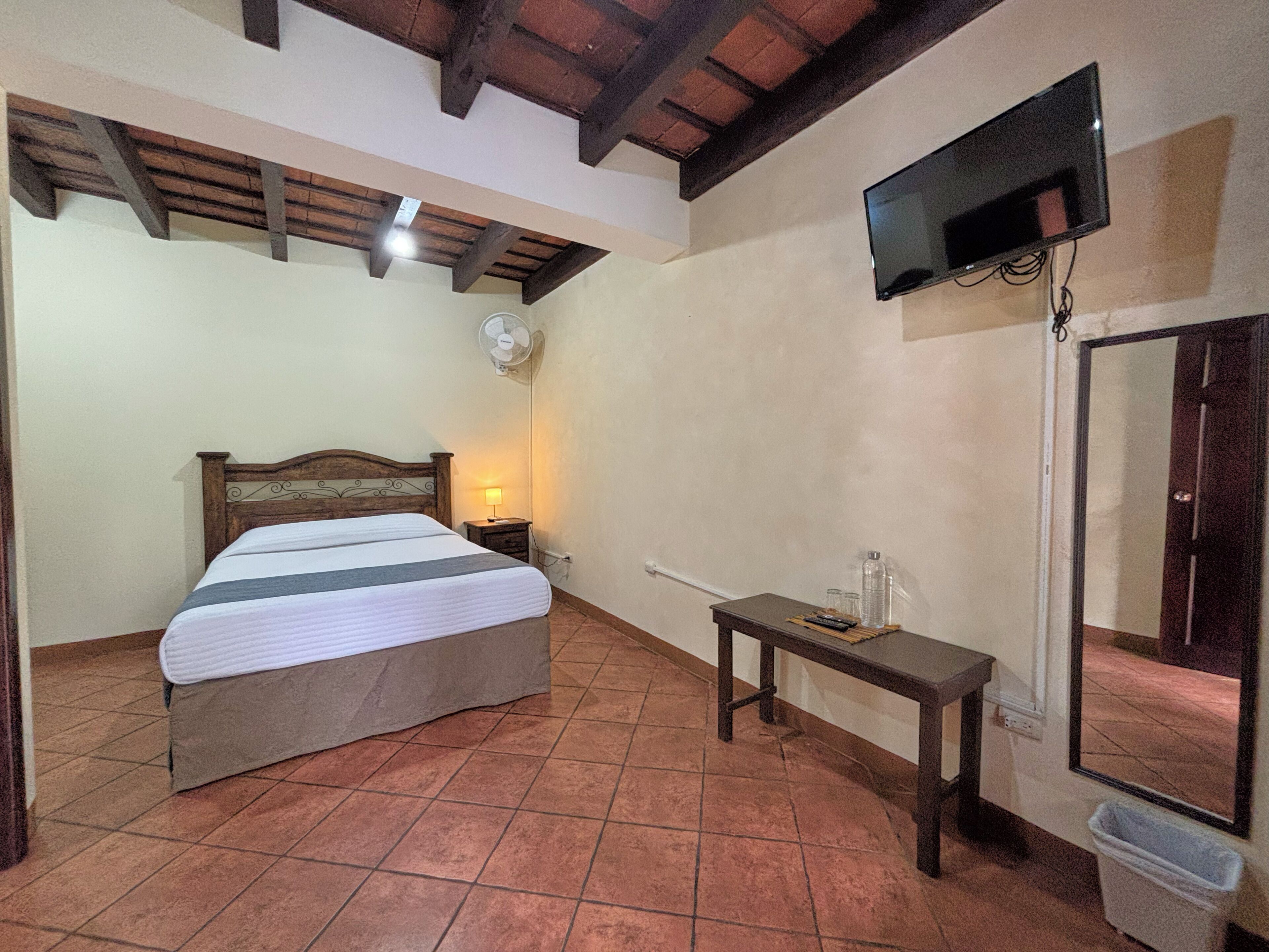 A bedroom with a bed, a bedside table, a wall-mounted TV, and a door.