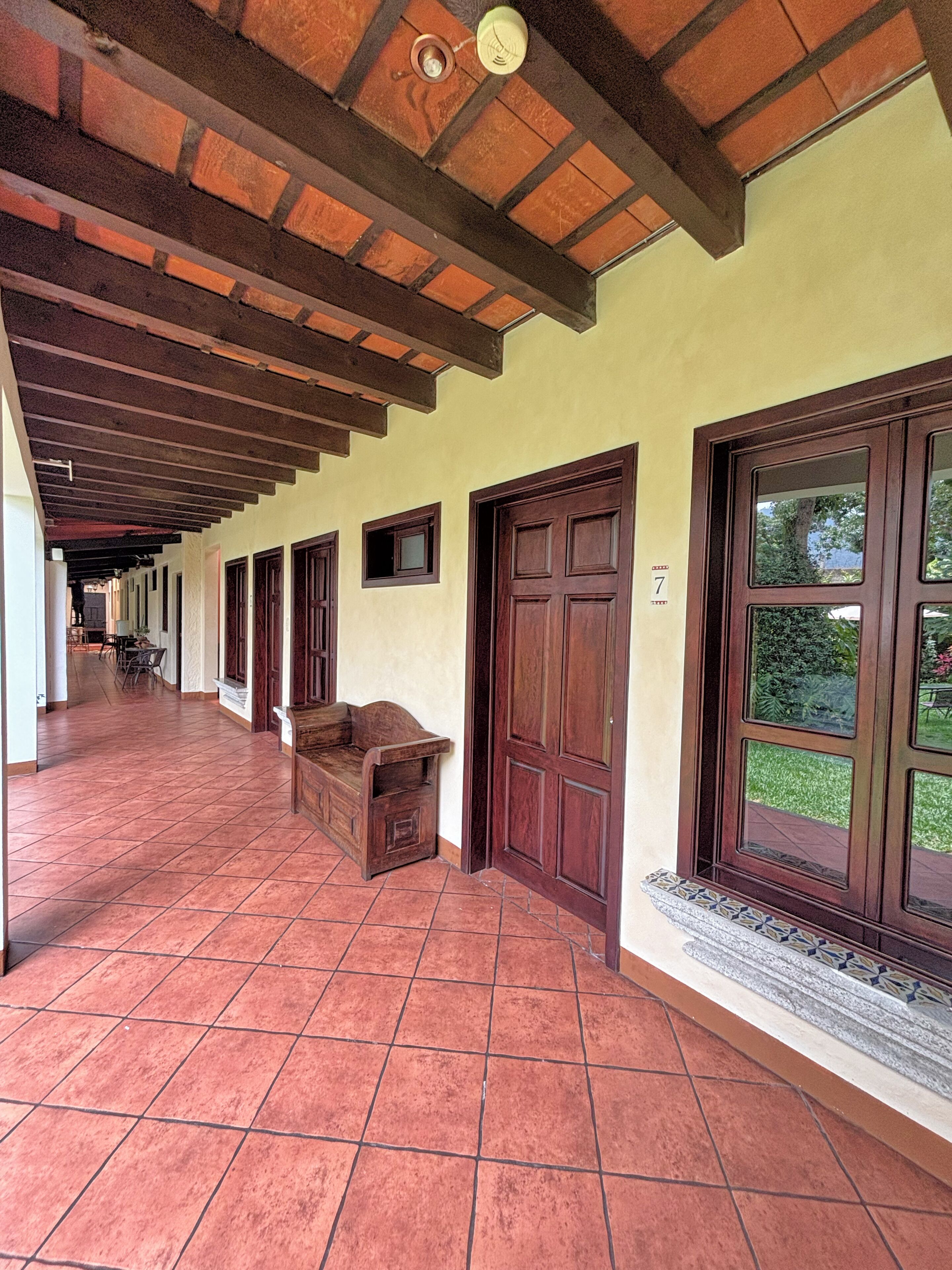 A corridor with tiled flooring, wooden doors, and a bench.