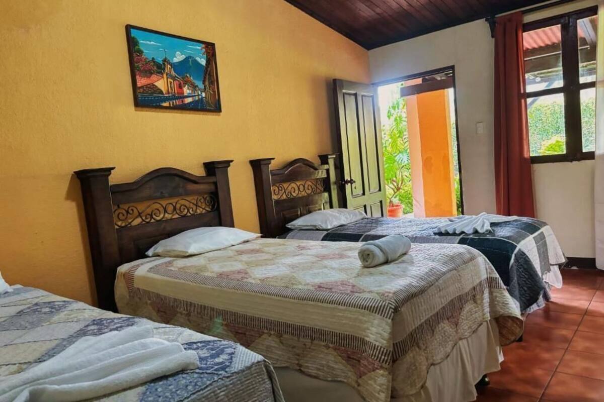 Ein Zimmer mit drei Betten, einer Holzbalkendecke, einem Bild an der Wand und einem Fenster mit Vorhängen.